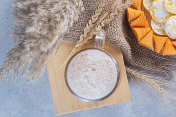 A glass of beer with wheat and potato chips on hay background