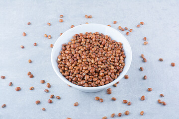 White bowl of red beans sitting in the middle of a scattered mess of beans on marble background