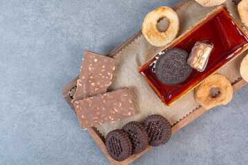 A wooden cutting board of cookies and piece of cake