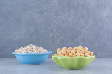 A bowl of raw chickpeas next to a bowl of cooked chickpeas on marble background