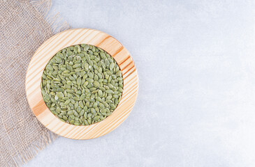 Dried, raw pepitas in a wooden plate next to pieces of fabric on marble background