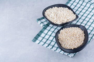 Bowl of short-grain rice and a bowl of oat on a towel on marble background
