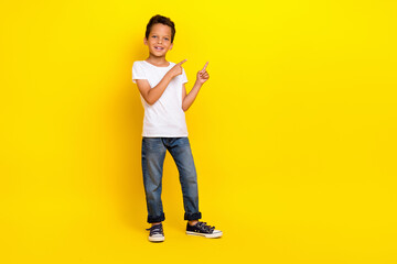 Fototapeta na wymiar Full body photo of small boy stand index promo wear t-shirt jeans sneakers isolated on yellow color background