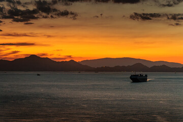 Fototapeta na wymiar Small cargo ship sails off coast at sunset