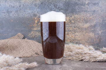 Glass of dark beer with ears of wheat on marble table