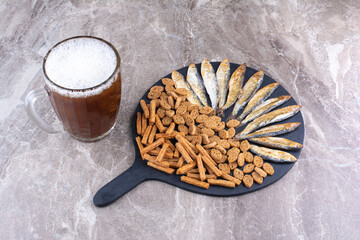 Various snacks and glass of beer on marble surface