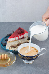 A hand pouring milk in cup of coffee on gray background