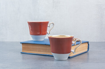 Two cups of coffee with book on gray background