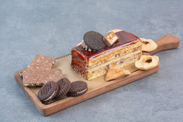 A wooden cutting board of cookies and piece of cake
