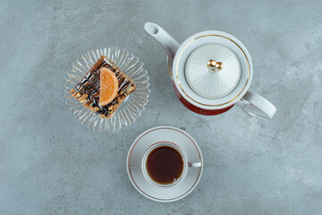Slice of cake on glass plate with glass of tea and teacup