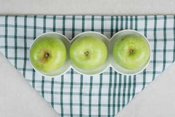 Whole green apples on white plates with striped tablecloth