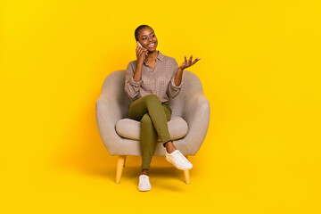 Photo of charming sweet woman wear plaid shirt sitting armchair communicating modern device empty space isolated yellow color background