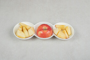 Red apple and slices in white bowls