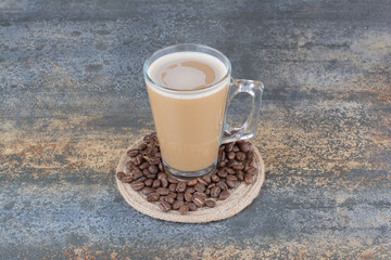 A cup of delicious coffee with coffee beans on marble background