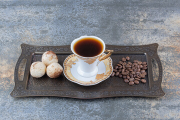 A cup of dark coffee with cookie on dark board
