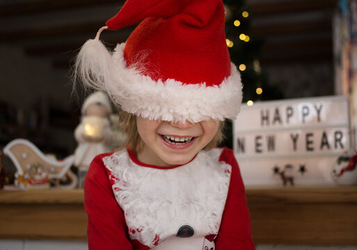 smiling happy child in a red santa hat, hid, pulling the hat over his eyes. The kid is waiting for a miracle. Christmas, New Year, merry family winter holidays concept
