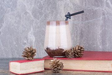 A cup of coffee with book and pinecones on marble background