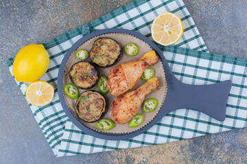 Roasted chicken legs with fried vegetables and lemon on dark board