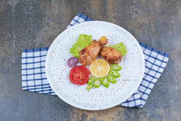 Grilled chicken drumsticks on white plate with vegetables