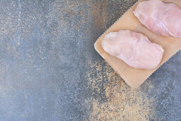 Uncooked chicken breasts on wooden board