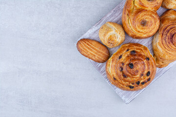 Various sweet pastries and rolls with cookies on wooden board
