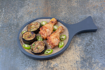 Grilled chicken legs with fried vegetables on dark board