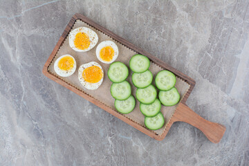 Sliced boiled eggs with cucumber on wooden board
