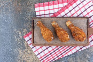 Grilled chicken drumsticks on wooden board with tablecloth