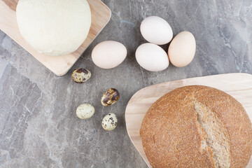 Chicken eggs with quail eggs and bread on marble background