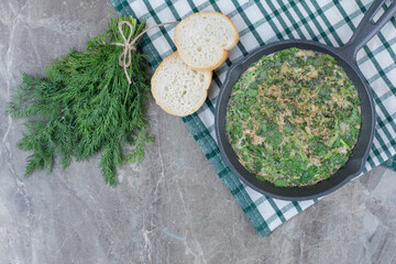 A dark pan of fried eggs with greens and white bread on tablecloth