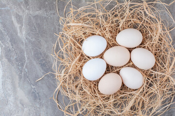 Several chicken fresh eggs on hay on marble background