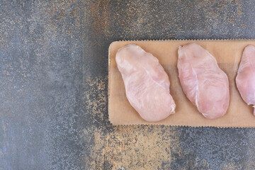 Uncooked chicken breasts on wooden board