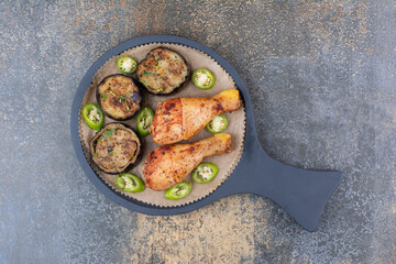 Grilled chicken legs with fried vegetables on dark board
