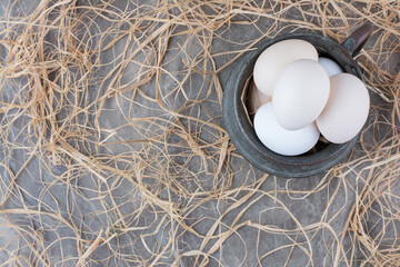 Fresh white chicken eggs in ancient cup on hay