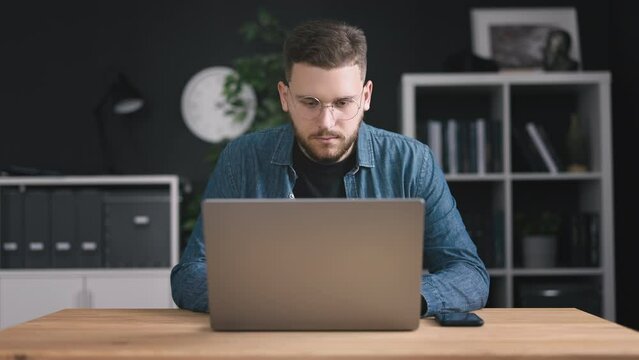 Young bearded programmer writing code on laptop, young man in eyeglasses focused on a computer