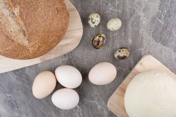 Chicken eggs with quail eggs and bread on marble background