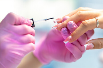Nail of a young girl or woman in selective focus on the background of a brush with a transparent varnish of a manicure master  - a manicurist in a beauty salon. Nail care during manicure procedure.
