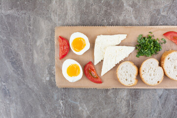 Delicious boiled eggs with sliced tomato and bread on wooden board