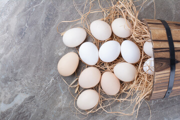Several white fresh eggs on hay on marble background