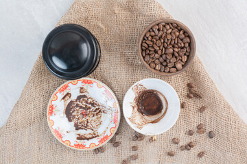 Bowl of coffee beans and saucers with coffee stain on burlap