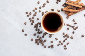 Cup of coffee, cinnamons and coffee beans on gray surface