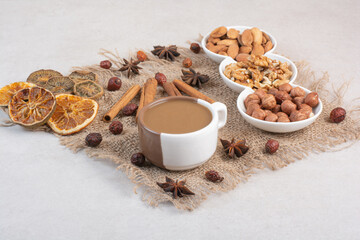 A cup of coffee with dried oranges and nuts on marble background
