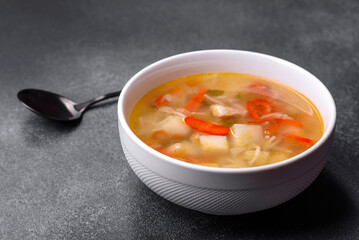 Closeup of a bowl of chicken noodle and vegetable soup on a concrete table