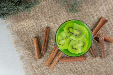 A glass of kiwi juice and cinnamon sticks on burlap
