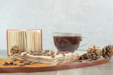 Cup of espresso, coffee beans and pinecones on wooden piece