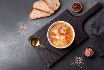 Closeup of a bowl of chicken noodle and vegetable soup on a concrete table
