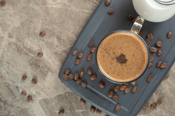 Cup of hot coffee and coffee beans on dark plate