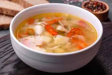 Closeup of a bowl of chicken noodle and vegetable soup on a concrete table