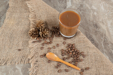 Glass of coffee with coffee beans and spoon on burlap