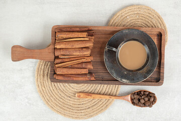 Cup of coffee with cinnamon sticks on dark board and coffee beans